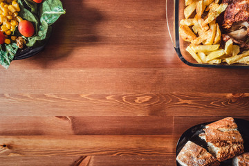 fondo de madera con ensalada, pollo y patatas fritas