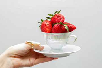 The cup for tea is filled with strawberries in the girls hand