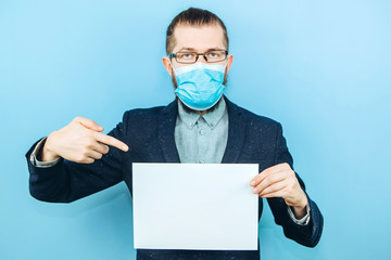 A man in a suit, glasses and a medical mask holds a piece of paper, on a blue background. Place for text. Businessman holds a tablet in his hands. The problem of business due to coronavirus. COVID-19