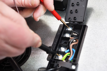 A professional electrician checks the connection quality, contact, voltage in the circuit of the cooking induction surface with the help of a tester. Troubleshooting in an electric stove.