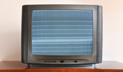 Old TV on a pedestal against the background of wallpaper. The noise on the screen.