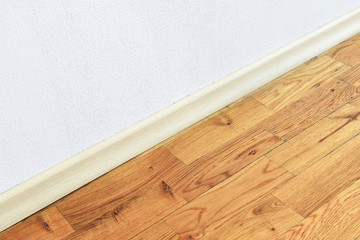 Wooden wall base skirting, finishing material with wood laminate floor and white mortar wall. Empty room with white wall and wooden floor.