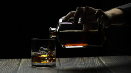 Pouring alcohol drink whiskey, cognac into glass. Black background. Silhouettes