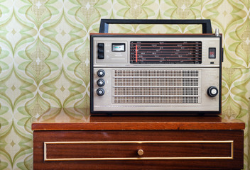 Antique radio receiver of an old nightstand in a vintage room with old-fashioned wallpaper, tinted and added noise