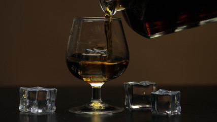 Pouring whiskey, cognac into glass. Brown background. Pour of alcohol drink