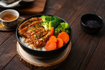 Japanese Food Style : Homemade Chicken Teriyaki grilled with rice , carrot , broccoli put on the black bowl and place on wooden table