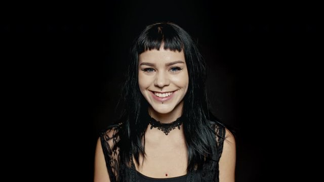Beautiful woman with pierced lips smiling against black background. Young gothic woman looking happy.
