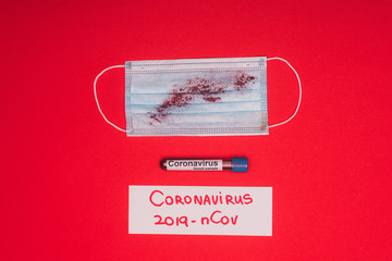 Top view of medical mask with blood near test tube with blood sample and card with coronavirus 2019-nCov lettering on red background