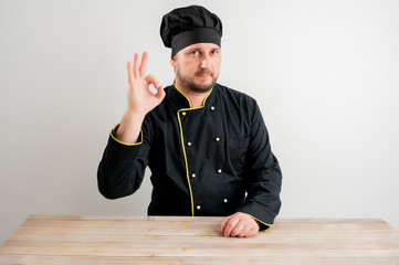 Young male chef in black uniform showing OK sign