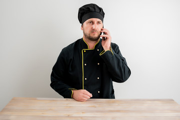 Young male chef in black uniform talking on cellphone
