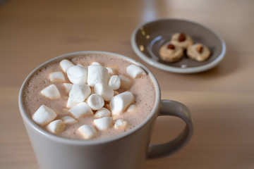 a dark Cup of coffee and marshmallows is placed on a wooden table. a plate of cookies in the background. the Bokeh. close up. copy space