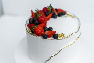 A beautiful white cake with cheese cream, meringues, chocolate and fresh Berries on a white background. The original idea for a wedding cake or birthday cake.