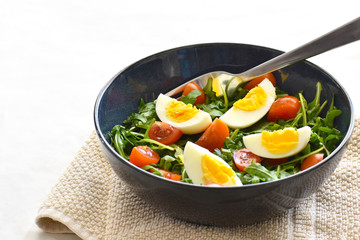 Egg salad with arugula or rocket, tomatoes.  Healthy and dietary food.  Selective focus.  Copy space is on the left side. 