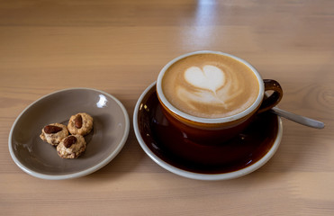 a dark Cup of coffee and marshmallows and a plate of cookies is placed on a wooden table. drawing of a heart on foam. love.. close up.
