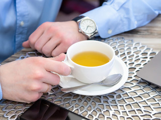 a businessman's hands hold a white Cup of green tea during lunch. the laptop is on the table. close up.