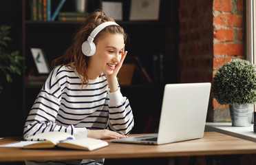 Excited woman in headphones having conversation on video chat while using laptop at home.