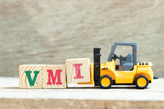 Toy forklift hold letter block I to complete word VMI (abbreviation of vendor managed inventory) on wood background