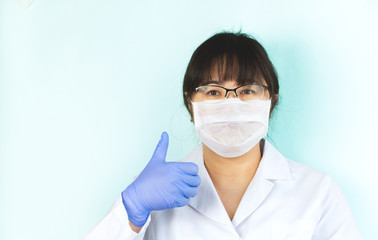 The woman is wearing a medical mask in a white uniform, protective blue gloves with a raised finger, everything will be fine