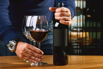 The culture of winemaking. Samelie offers wine, the hands of a winemaker with a glass of wine and an uncorked bottle, winemaking, a culture of drinking alcohol, and a distillery.