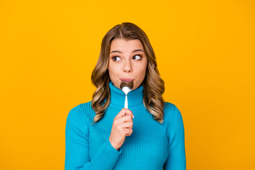 Photo of charming funny curly lady hold metal spoon in mouth look tempting empty space dream of tasty food dinner wear blue turtleneck isolated bright shine yellow color background