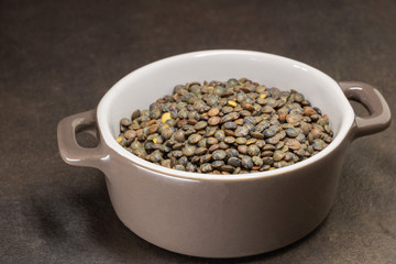 Lentilles vertes du Puy crues dans une marmite en céramique sur fond noir