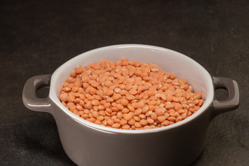 Lentilles corail crues dans une marmite en céramique sur fond noir