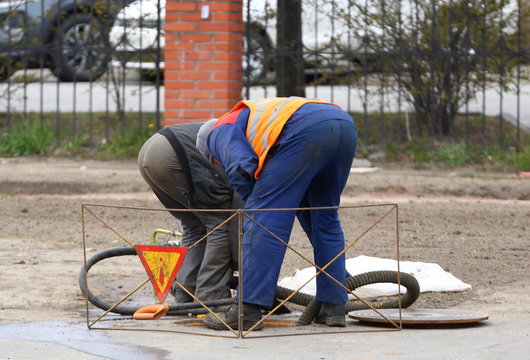Two workers bent over a manhole in the street