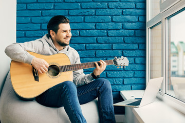 happy man smiling and playing on guitar at home with laptop