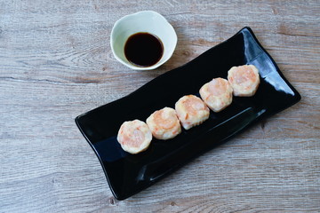 steamed Chinese dumpling topping shrimp on black plate dipping soy sauce