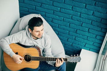 romantic guitarist with pretty smile playing on guitar and dreaming in the modern room