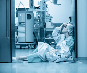 Concept of medecine surgery, Kovid 19. Tired, exhausted doctor after an exhausting shift in the intensive care unit. Pandemic, isolation, epidemic hard work of doctors, stay home. Blue monochrome - obrazy, fototapety, plakaty