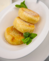 Round curd cheesecakes. Serving homemade food on a white plate. Cheesecake with mint for breakfast, a serving of three. High calcium appetizing healthy food.