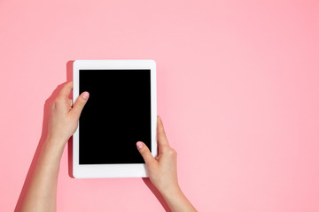 Hand using tablet, device on top view, blank screen with copyspace, minimalistic style. Technologies, modern, marketing. Negative space for advertising. Coral color on background. Stylish, trendy.