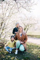 Fototapeta premium Happy mother and her two children is standing on a background blossoming Apple-trees and cherries