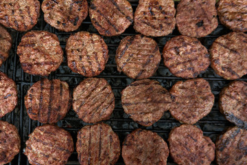 Big amount of grilled beef burgers. Lot of burgers on grill. Fast food element grilled for hamburgers. Cooking food outdoor. Open air grill station. Fast food festival. Summer party.Close up top view
