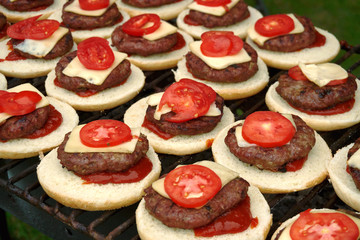 Close up of cheeseburgers on hot barbeque stand outdoor. Burger made of white bun, beef cutlet, slice of cheese and tomato with ketchup added. Hot cheeseburgers on grill ready to be served for eating