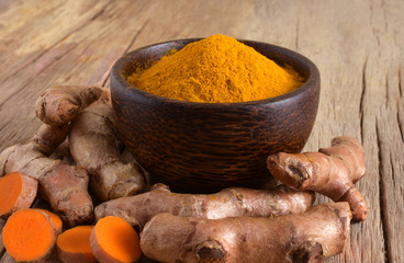 Turmeric (curcumin) powder in  wooden bow and fresh turmeric rhizome on a wooden background.
