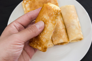 pancake with curd rolled into a roll in hand on a background a plate with pancakes. Close-up.