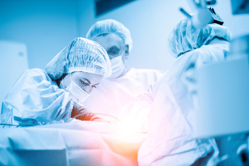 Female surgeon with operating assistants. Surgeons during work. Blue filter. Modern medicine with professional doctors.