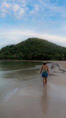 Thai woman in shorts and hat walking barefoot on beach at low tide