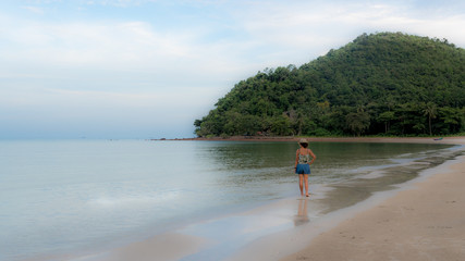 Thai woman in shorts and hat walking barefoot on beach at low tide