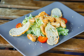 Fresh healthy Caesar salad on a ceramic grey plate on a wooden background.