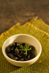 Black small olives in a ceramic bowl on rustic table