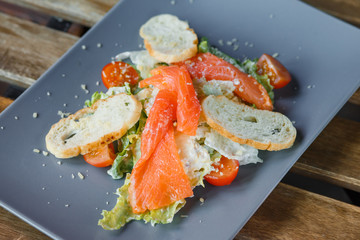 Fresh healthy Caesar salad with salmon on a ceramic grey plate on a wooden background.
