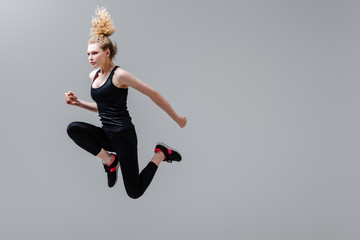 curly sportswoman in sportswear jumping isolated on grey