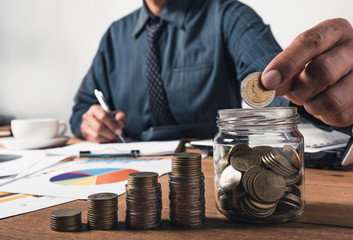 Business man working and writing on notebook with stack of coins for financial and accounting concept.