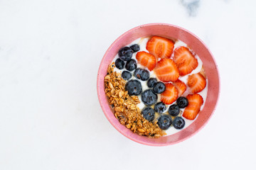 Bowl of homemade granola with yogurt, strawberry and fresh blueberries on marble background top view