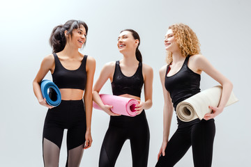 happy and multicultural women holding fitness mats on white