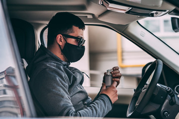 man in a black medical mask. handsome brunette driving an expensive car. antiseptic gel disinfects hands. thief, steal, coronavirus, disease, infection, quarantine, medical mask, covid-19