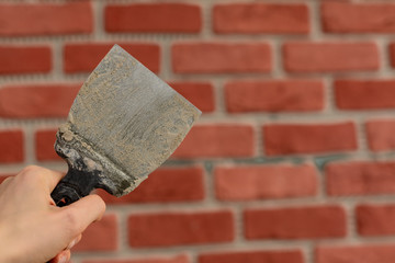 The master's hand is holding putty knife patchingwith traces of concrete mortar on the background of a red brick wall. Renovation and repair process.
